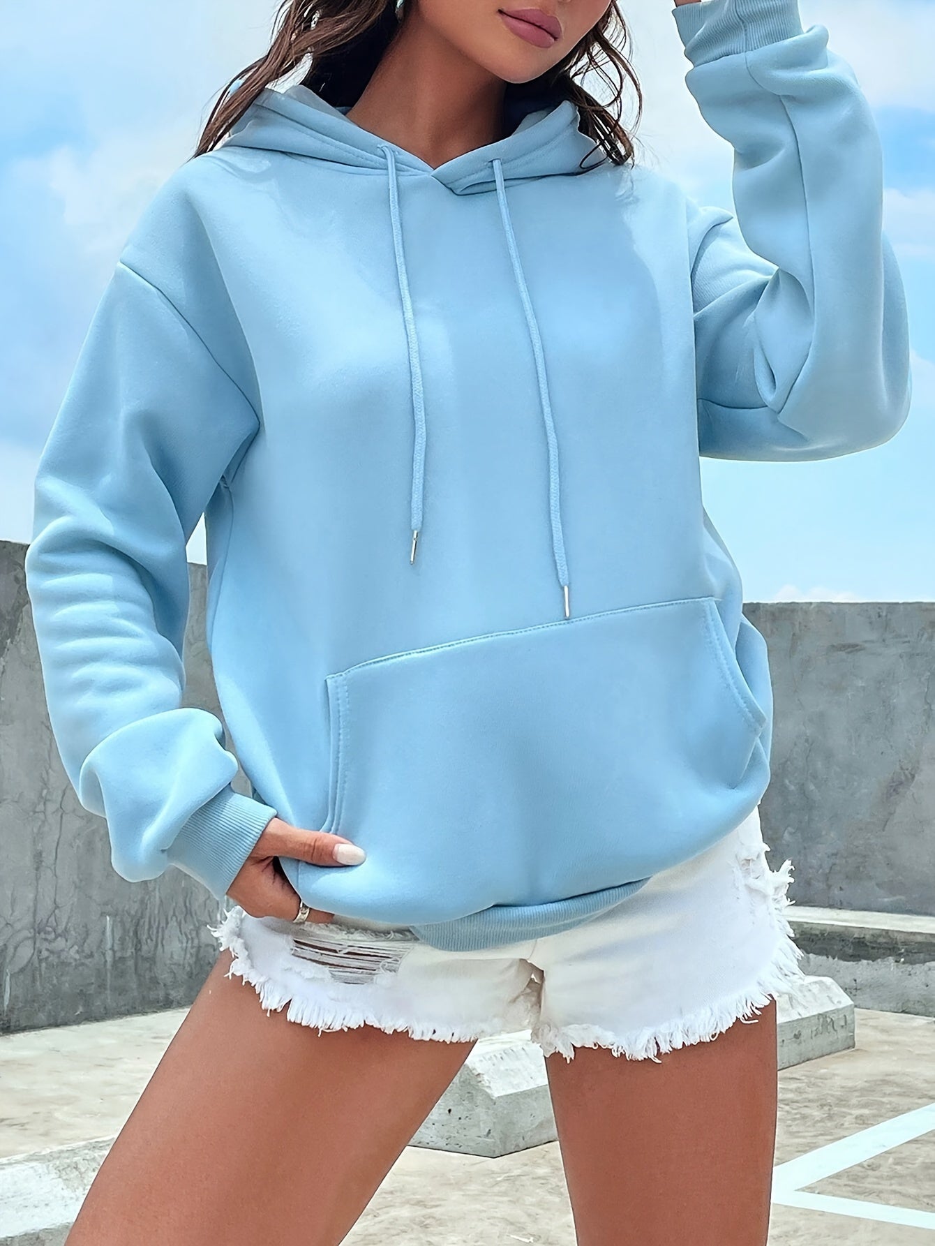 Frau in hellblauem Hoodie und weißen Jeansshorts auf Dachterrasse.