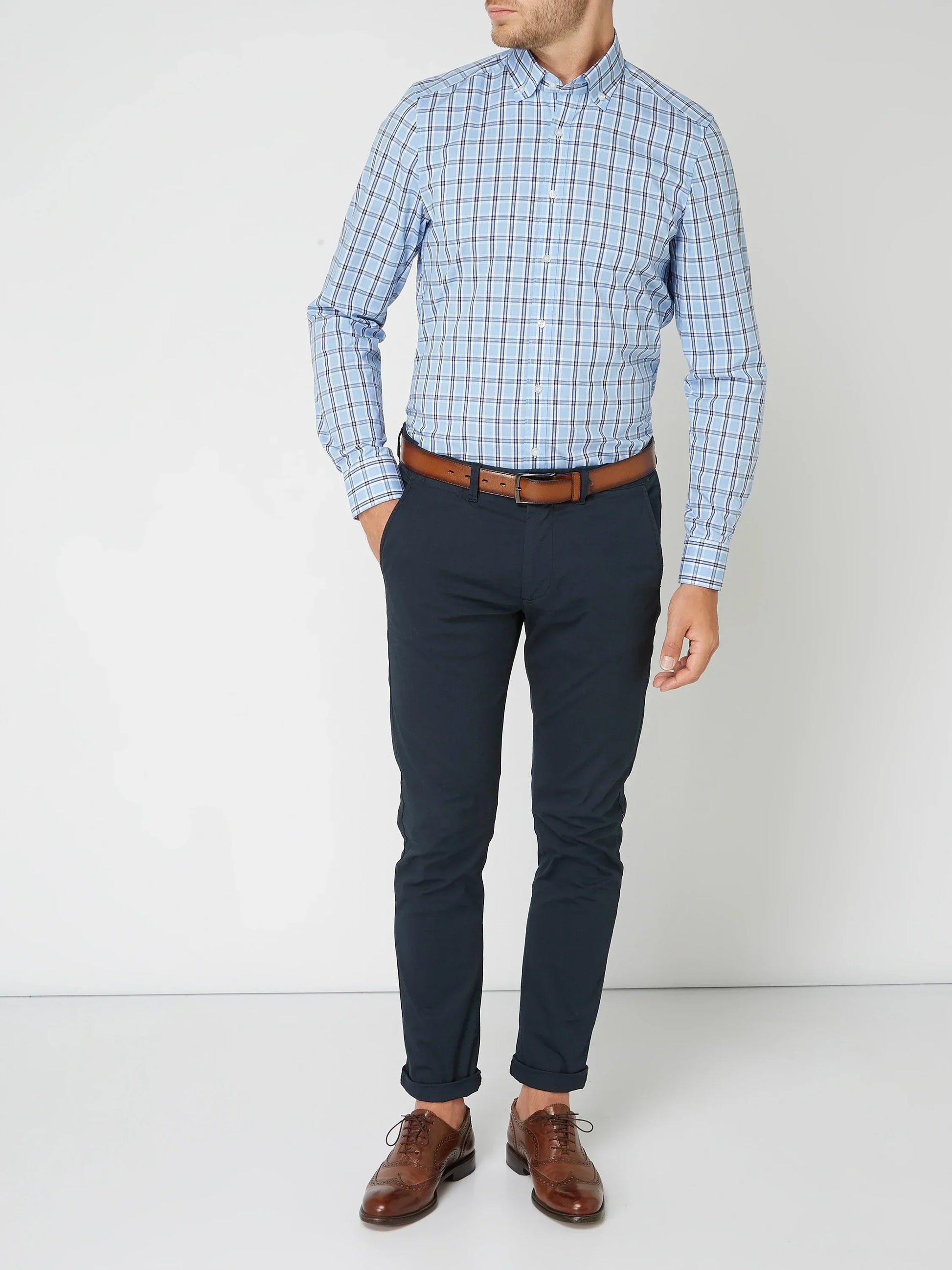Mann in kariertem Hemd und blauer Hose, brauner Ledergürtel, elegante braune Lederschuhe.