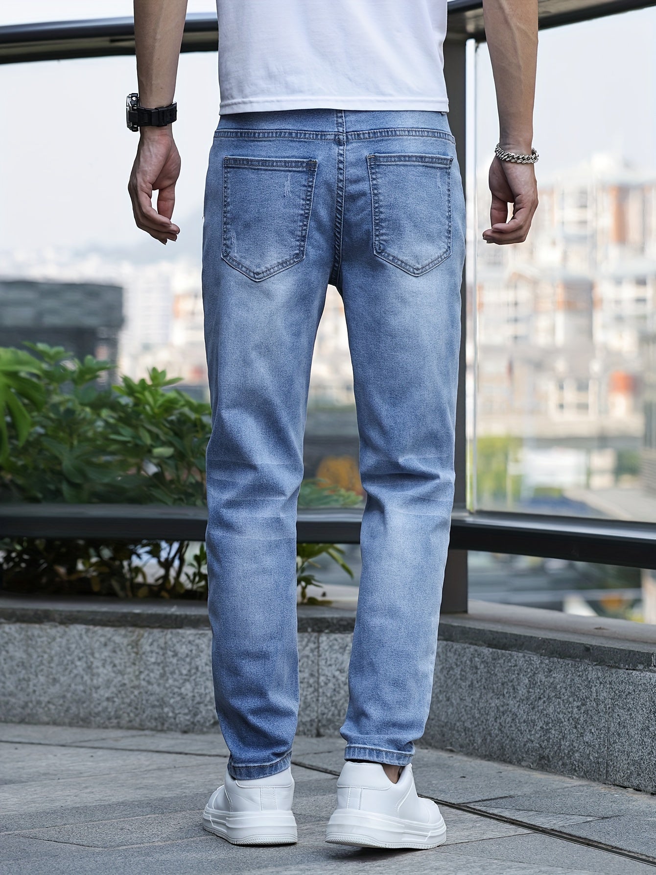 Mann in hellblauer Jeans und weißen Sneakers, Rückansicht, urbaner Hintergrund.