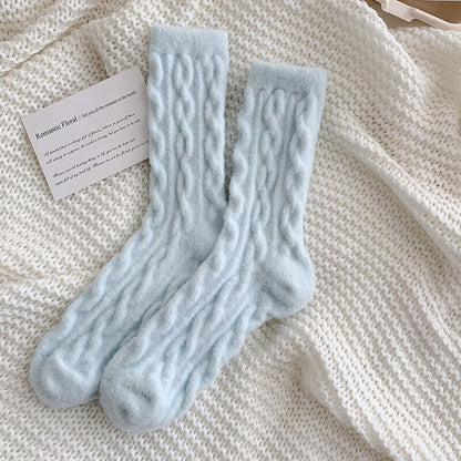 Hellblaue, gestrickte Wollsocken auf cremefarbenem Strickhintergrund mit Karte.