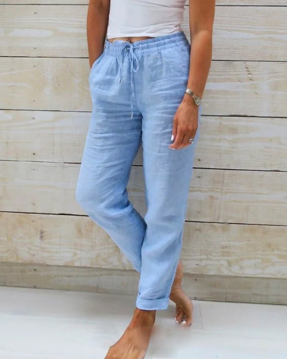 Frau trägt hellblaue Leinenhose mit Kordelzug, lässig, bequem, Sommermode, Holz-Hintergrund.