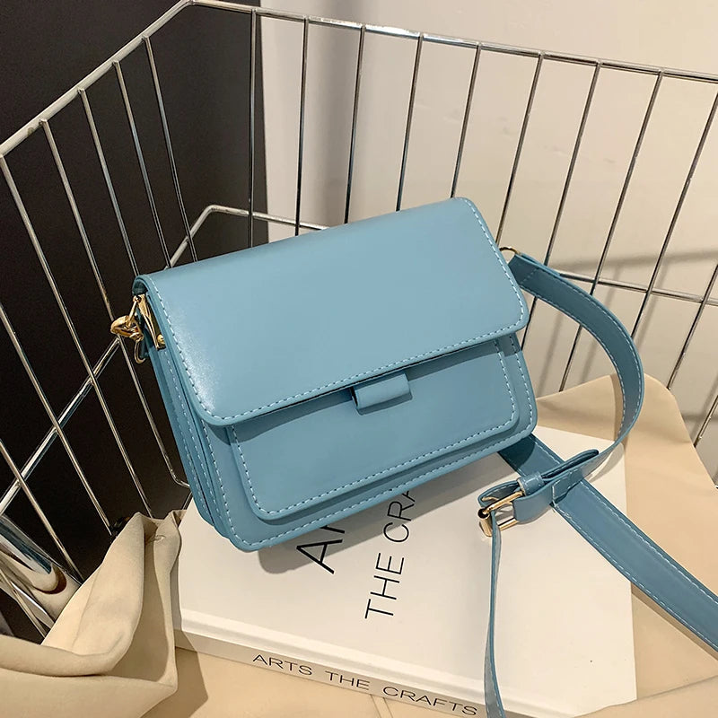 Blaue Umhängetasche aus Leder auf weißem Buch, stilvolles Accessoire für Damen.