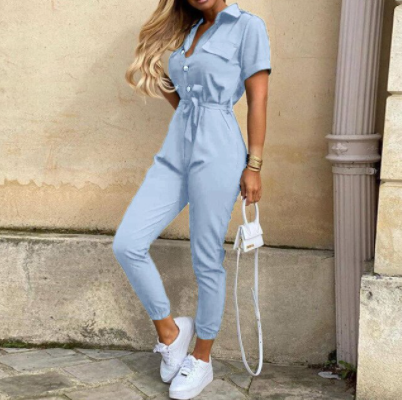 Frau in hellblauem Jumpsuit, weiße Sneakers, kleine weiße Handtasche, modisch, lässig.