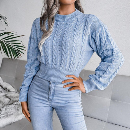 Frau in hellblauem Zopfmuster-Pullover und Jeans auf grauem Sofa, modisch, gemütlich.