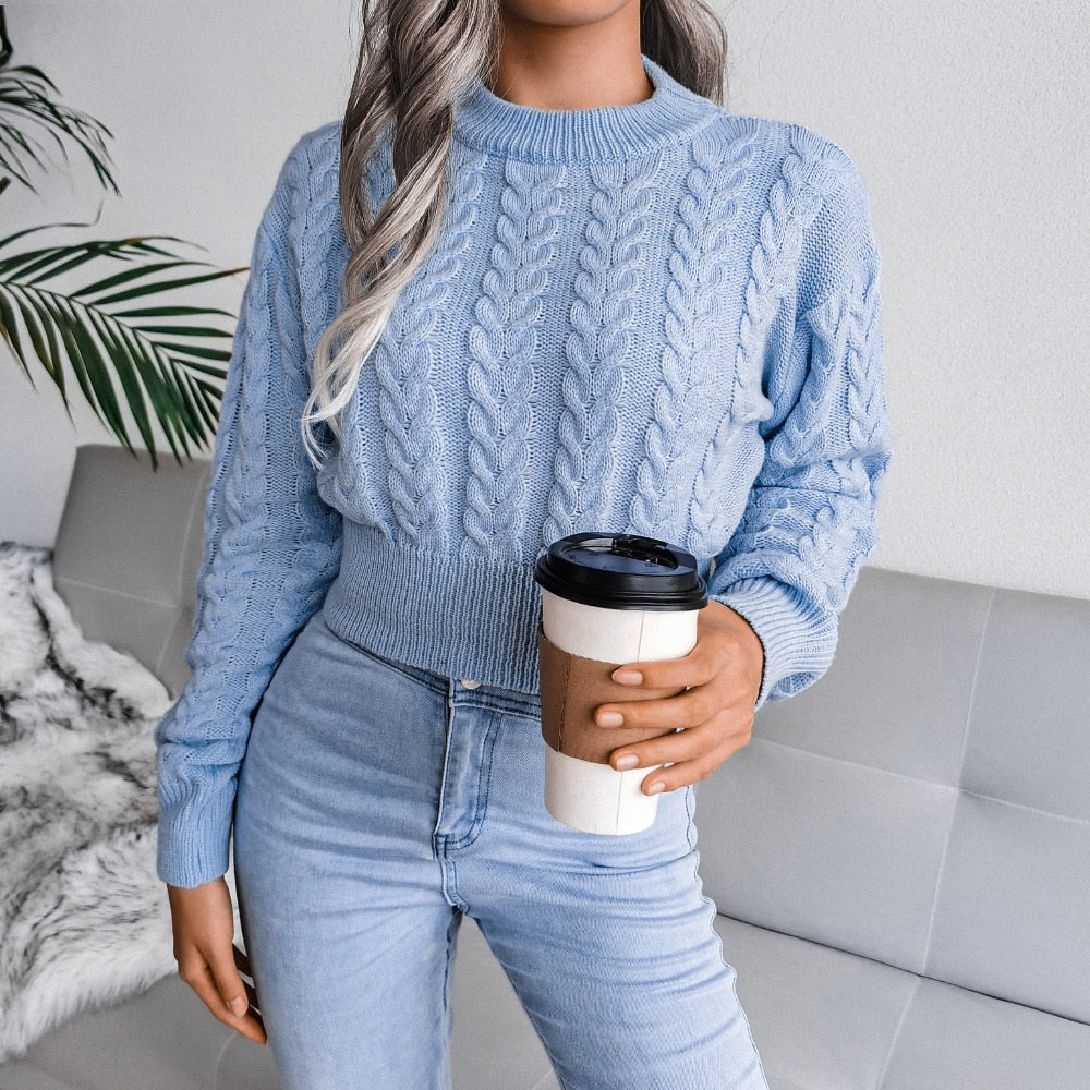 Frau in hellblauem Strickpullover hält Kaffeebecher, sitzt auf grauem Sofa.
