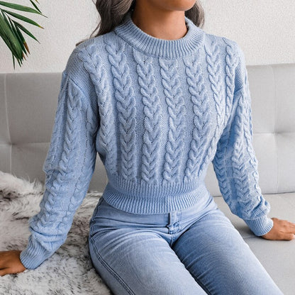 Frau in hellblauem Zopfmuster-Pullover und Jeans auf Sofa sitzend.