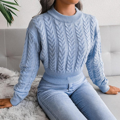 Frau in hellblauem Zopfmuster-Pullover und Jeans auf grauem Sofa, modisch, gemütlich.