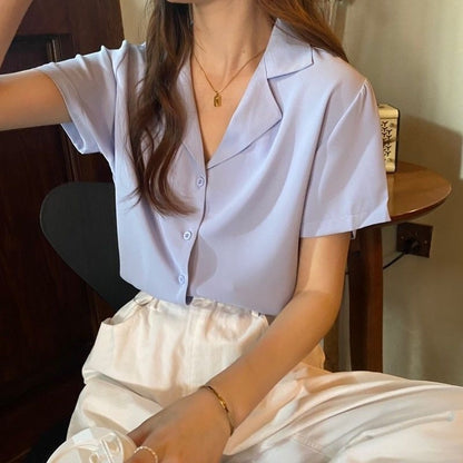 Frau in hellblauer Bluse und weißer Hose, sitzt entspannt, modisch, lässiger Stil.