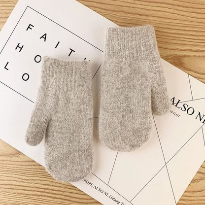 Hellgraue Strickhandschuhe aus Wolle auf Holztisch, warm und weich für den Winter.