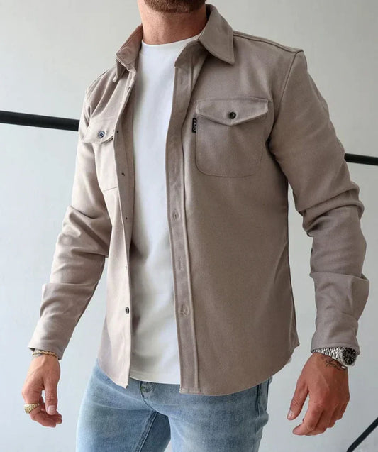 Mann in beiger Hemdjacke aus Baumwolle, weißem T-Shirt und blauer Jeans, lässiger Stil.