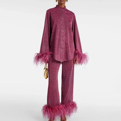 Modell i vinröd glittrig skjorta med ståkrage och byxor, båda med rosa fjäderkant, håller en liten guldfärgad väska. 1
