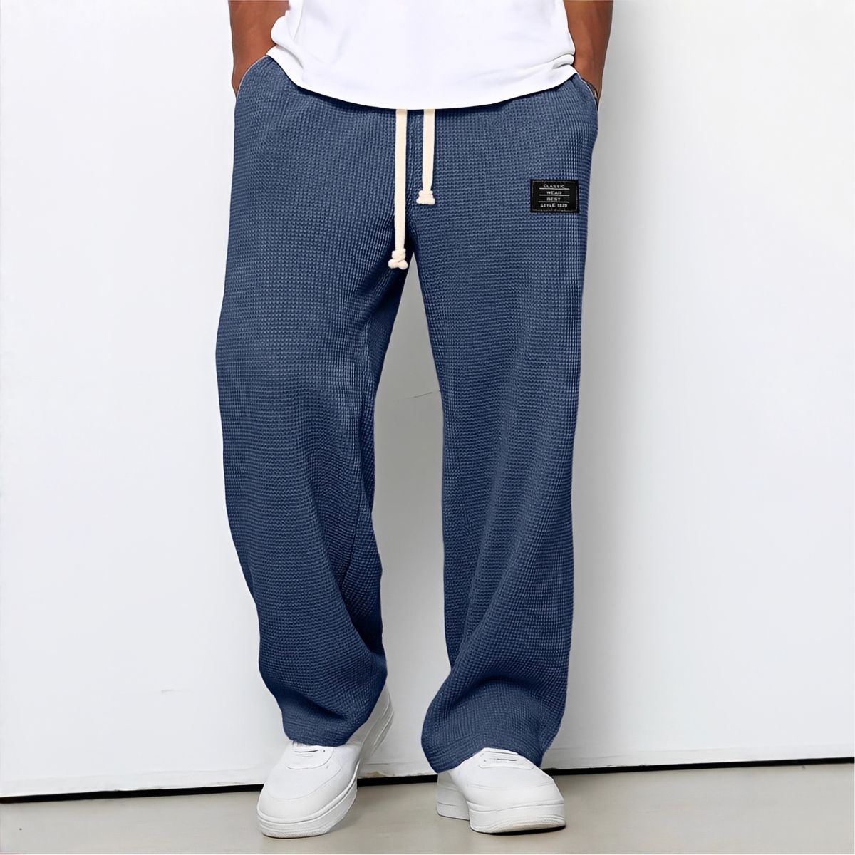 Modell i blå vaffelstickade byxor med vit dragsko, vit t-shirt och vita sneakers, framifrån 5