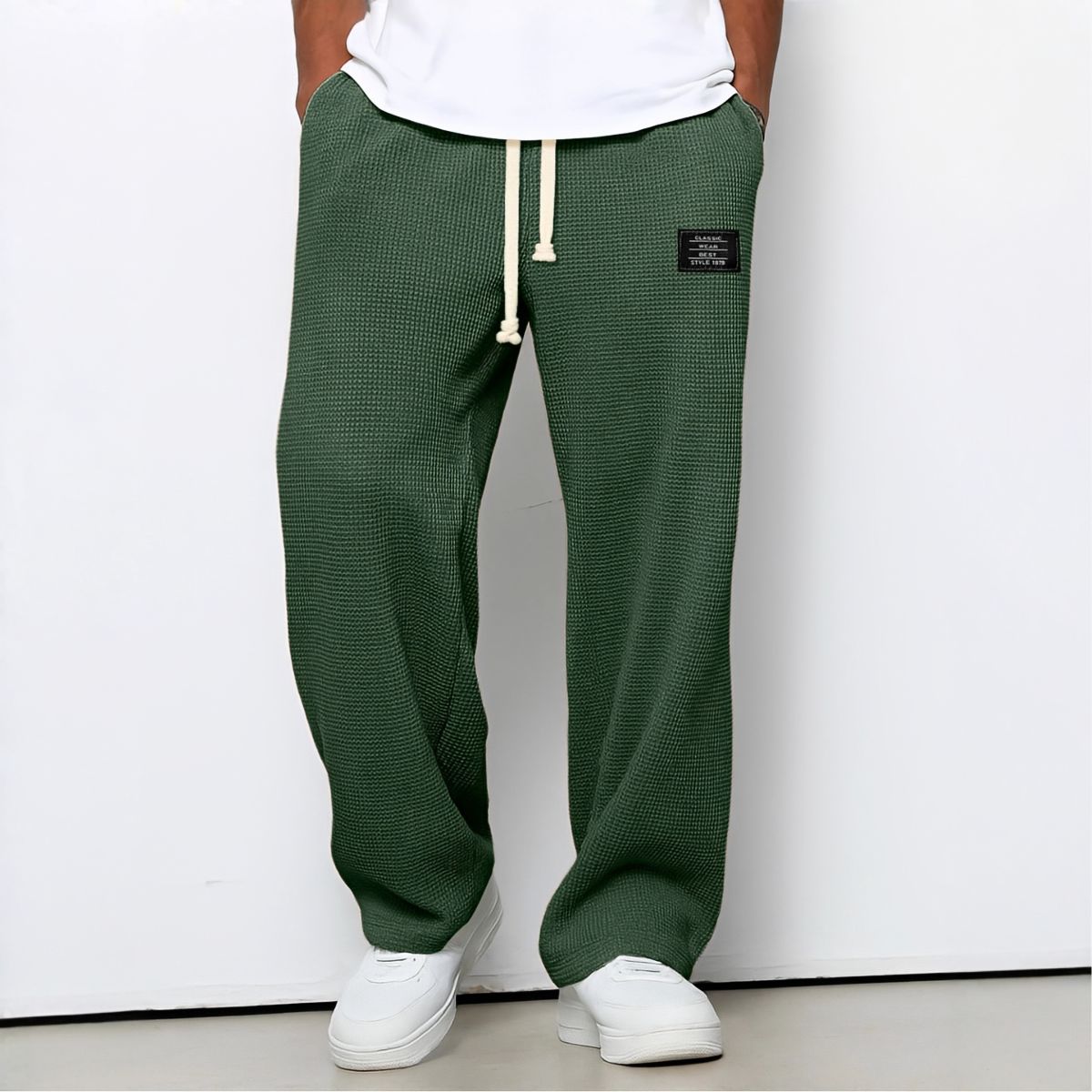 Modell i gröna vaffelstickade byxor med vit dragsko, vit t-shirt och vita sneakers, framifrån 4