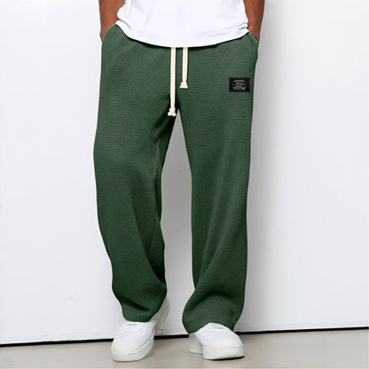 Modell i gröna vaffelstickade byxor med vit dragsko, vit t-shirt och vita sneakers, framifrån 4