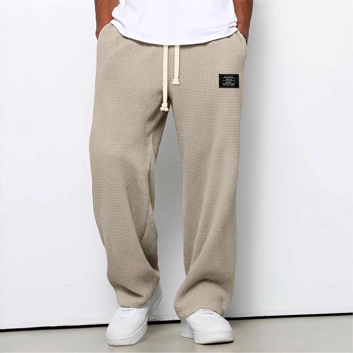 Modell i beige vaffelstickade byxor med vit dragsko, vit t-shirt och vita sneakers, framifrån 7