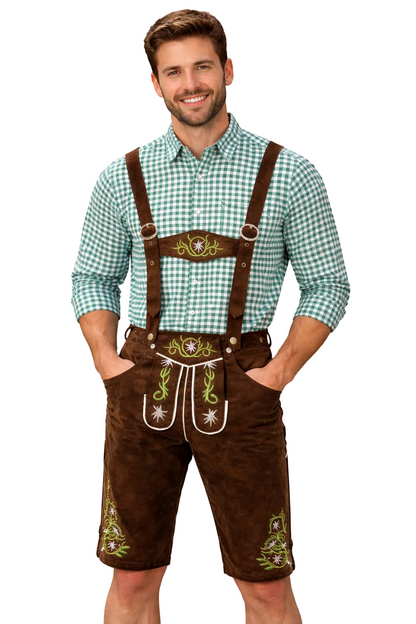 Leende man mot vit bakgrund i bruna lederhosen med broderade blomsterdetaljer, hängslen och grönrutig skjorta, händerna i fickorna. 1