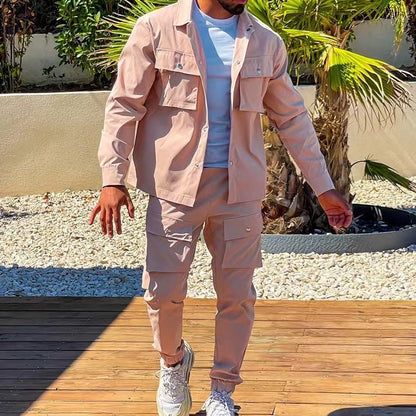 Mann in rosa Cargo-Anzug und weißen Sneakers im Freien vor Palmen.