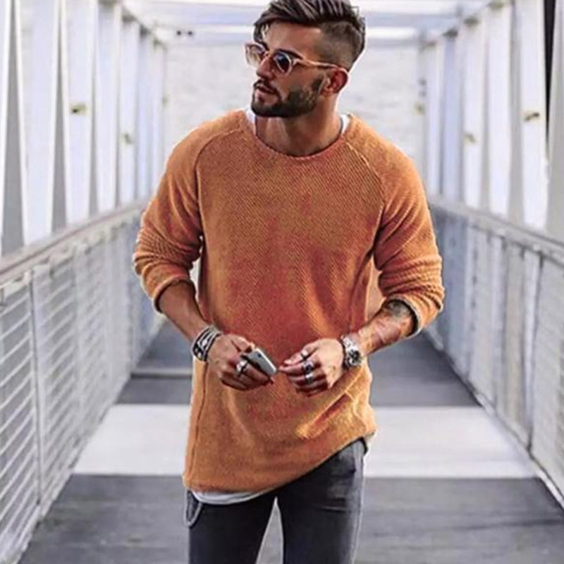 Mann mit orangefarbenem Pullover, Sonnenbrille und Jeans auf Brücke, modischer Freizeitlook.
