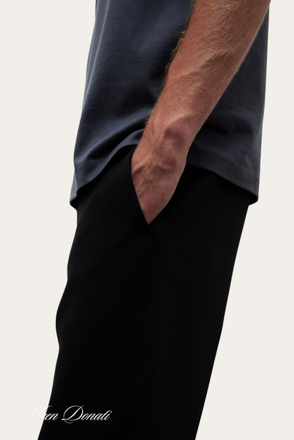 Mann in dunkelblauem T-Shirt und schwarzer Hose, Hand in Hosentasche, lässiger Stil.