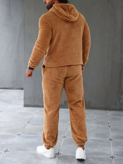 Mann in braunem Teddy-Fleece-Trainingsanzug, Kapuzenjacke, Jogginghose, weiße Sneaker.