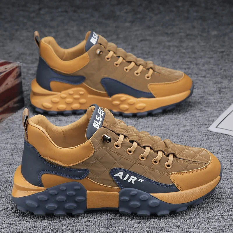 Braune und graue Herren-Sportschuhe, atmungsaktiv, mit Luftkissen-Sohle auf grauem Teppich.