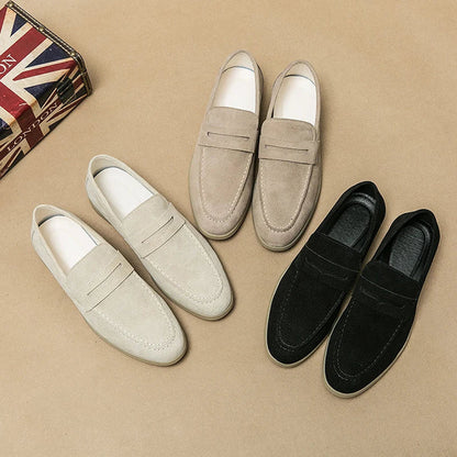 Drei Paar Herren-Slipper aus Wildleder in Beige, Sand und Schwarz auf braunem Hintergrund.