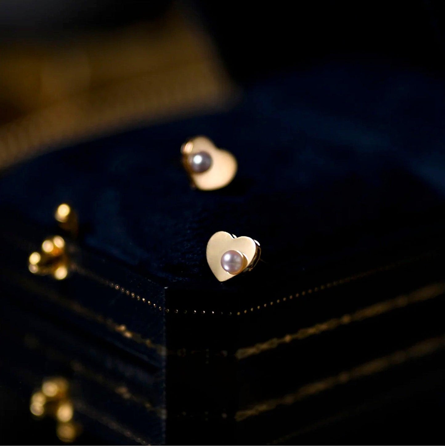 Goldene Herz-Ohrringe mit Perle auf schwarzem Hintergrund, eleganter Schmuck, Damenaccessoire.