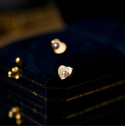 Goldene Herz-Ohrringe mit Perle auf schwarzem Hintergrund, eleganter Schmuck, Damenaccessoire.