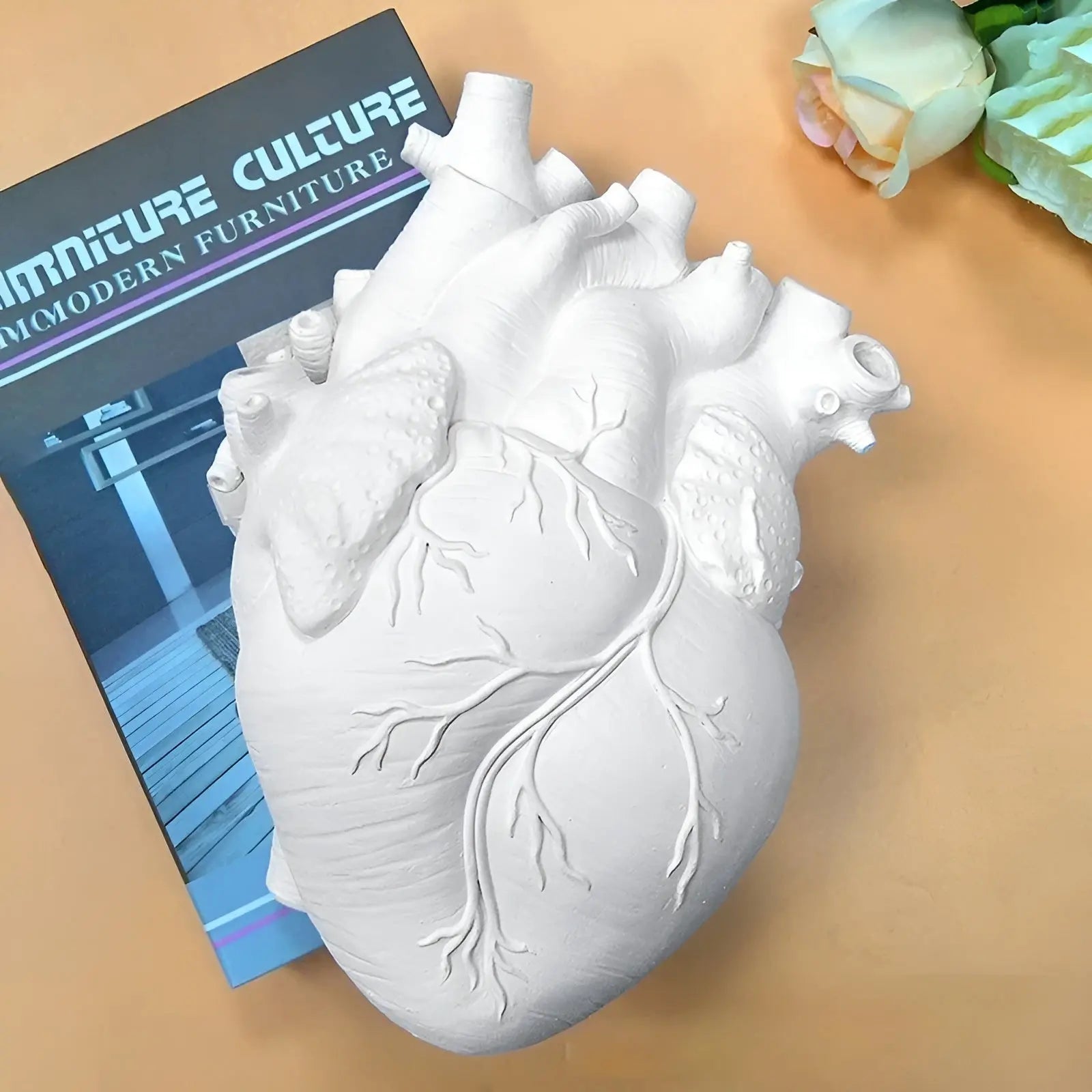 Weiße Herzskulptur aus Keramik auf Tisch, neben Möbelkatalog und Rose.