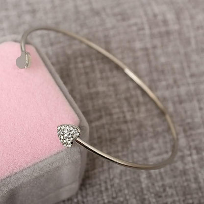 Silbernes Herzarmband mit Strasssteinen auf rosa Kissen, eleganter Schmuck für Damen.