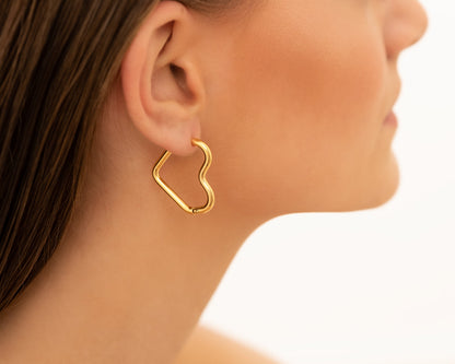 Frau mit goldenen Herz-Ohrringen, modischer Schmuck, elegantes Design, Nahaufnahme.