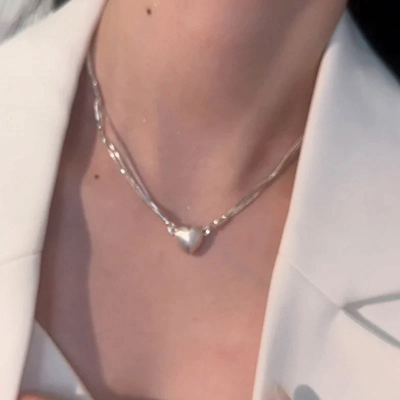 Silberne Herz-Halskette auf weißem Blazer, eleganter Schmuck für Damen.