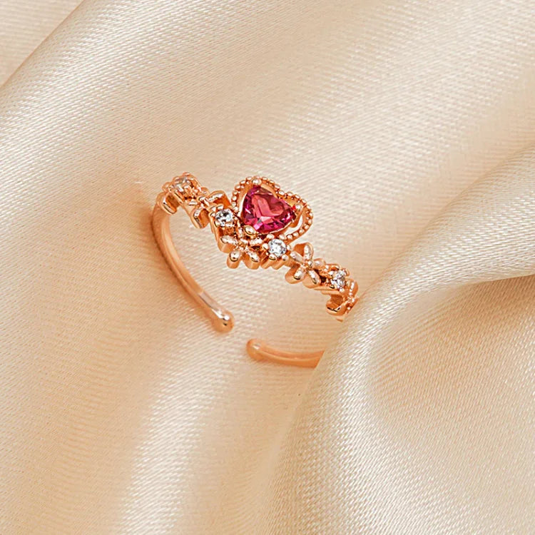 Roségoldener Herzring mit rosa Stein und Zirkonia, verstellbar, auf beigem Stoffhintergrund.