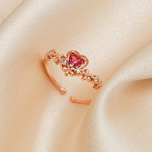 Roségoldener Herzring mit rosa Stein und Zirkonia, verstellbar, auf beigem Stoffhintergrund.