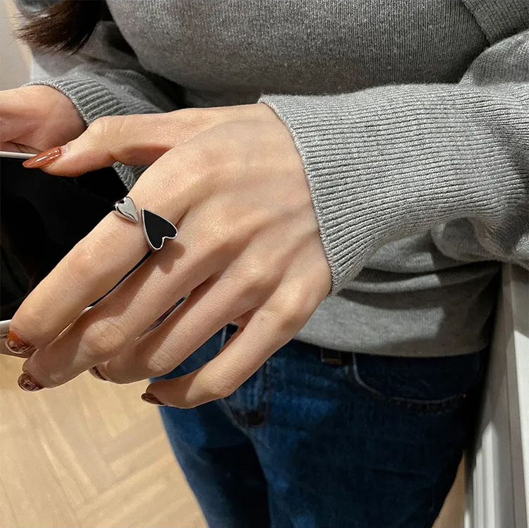 Frau mit grauem Pullover trägt schwarzen Herzring, hält Smartphone in der Hand.