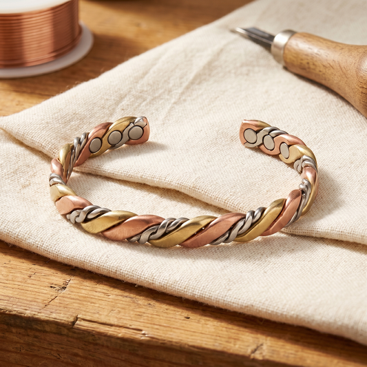 Flätat öppet armband i rosékoppar, gul mässing och silverton på linnetyg, med trådrulle bredvid 1