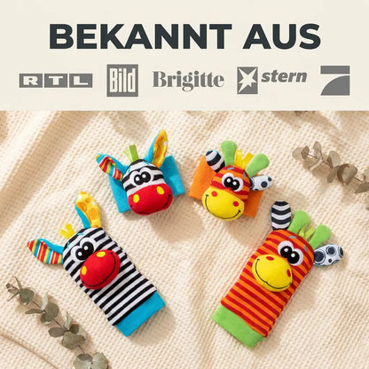 Fyra mjuka djurrassel, tv\u00e5 handledsband och tv\u00e5 sockor, ligger p\u00e5 en vaffelfilt med eukalyptusgrenar runtomkring. 7