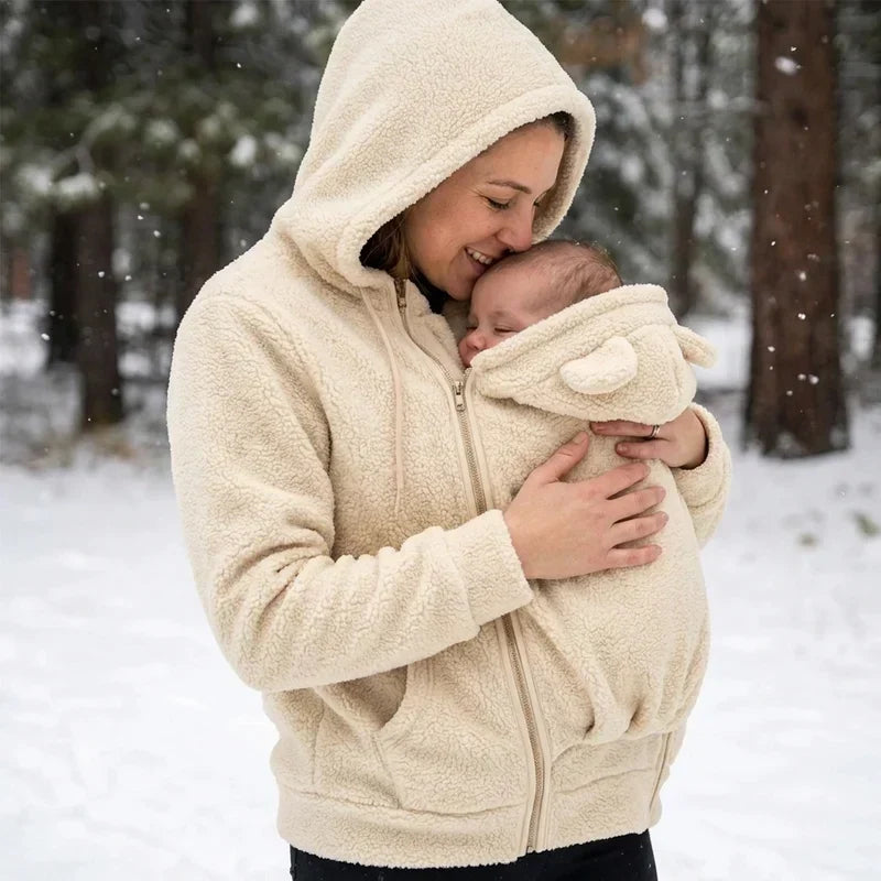 Kvinna i beige fleecehoodie kysser sin bebis i pannan i panelen med björnöron, ute i snöigt landskap. 8