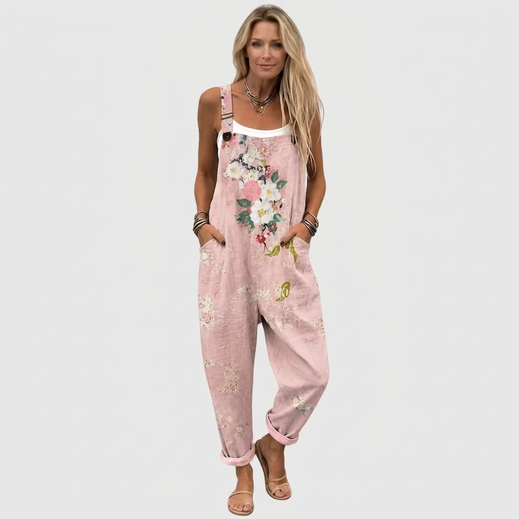 Hel figur framifrån: modell i hängselbyxorna över vitt linne, med blommönster, knäppta axelband, händerna i fickorna och sandaler. 2