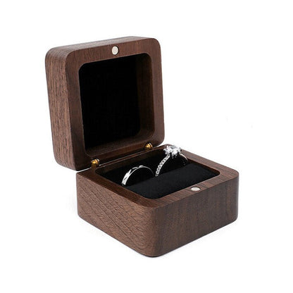 Offene Holz-Ringbox mit schwarzem Innenfutter, enthält zwei silberne Ringe.