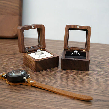 Zwei Holz-Ringboxen mit Glasdeckel auf Holztisch, eine mit silbernem Ring, eine mit schwarzem Ring.