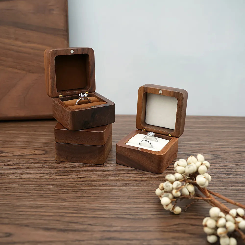 Zwei hölzerne Ringboxen auf Holztisch, eine offen mit Ring, dekorative Beeren im Vordergrund.