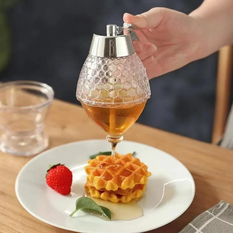 Hand hält Honigspender aus Glas, gießt Honig auf Waffeln, mit Erdbeere auf weißem Teller.
