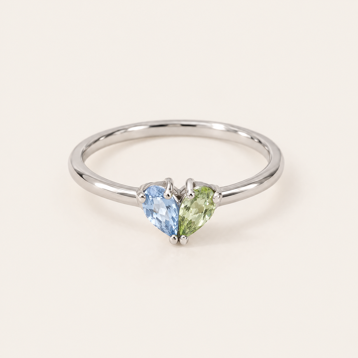 Silverfärgad ring framifrån med en ljusblå och en grön droppformad sten som tillsammans formar ett hjärta. 5