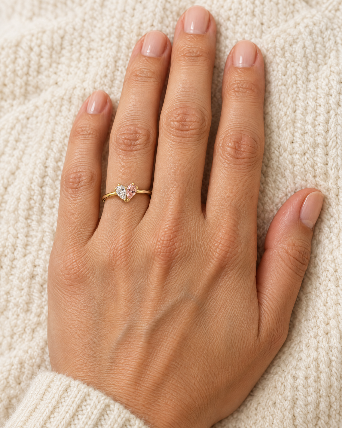 Ringen med klar och rosa sten på en hands långfinger, vilande mot en vit stickad tröja. 2
