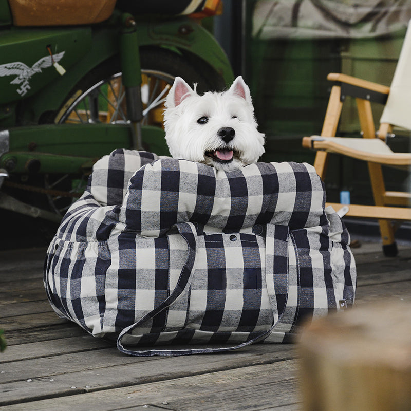 Weißer Hund in kariertem Hundebett auf Holzterrasse, gemütlich und stilvoll.