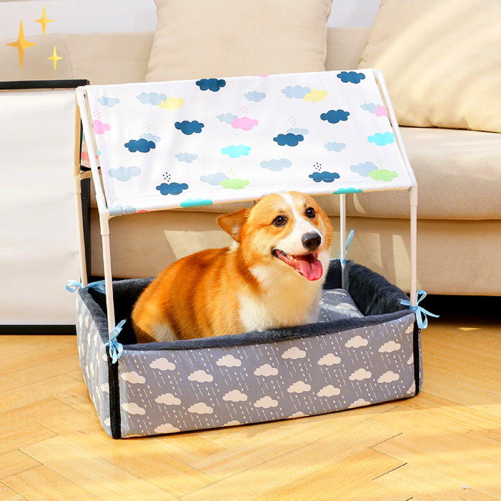 Corgi in einem bunten Hundebett mit Dach, Wolkenmuster, auf Holzboden, gemütlich und fröhlich.