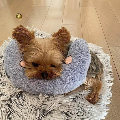 Kleiner Hund auf grauem, flauschigem Kissen auf Holzboden, gemütlich liegend.