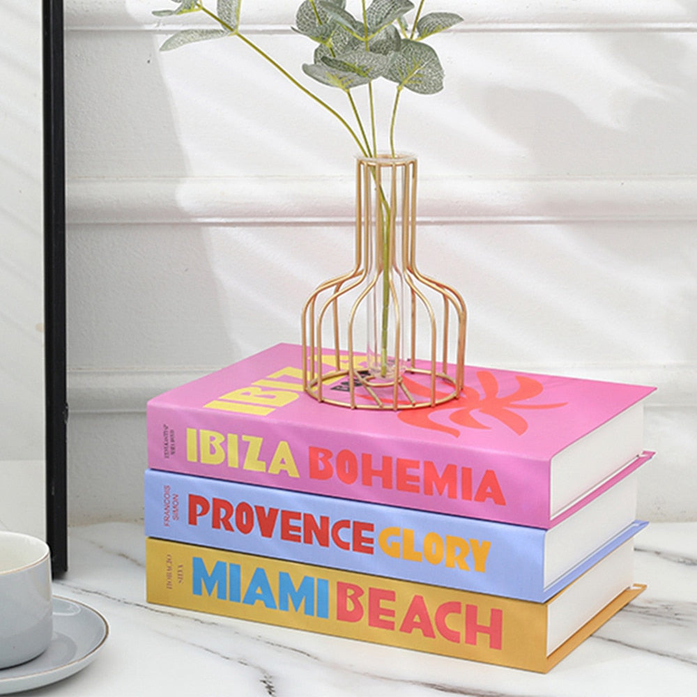 Drei bunte Bücher mit dekorativer Vase auf Marmortisch, Ibiza Bohemia, Provence Glory, Miami Beach.