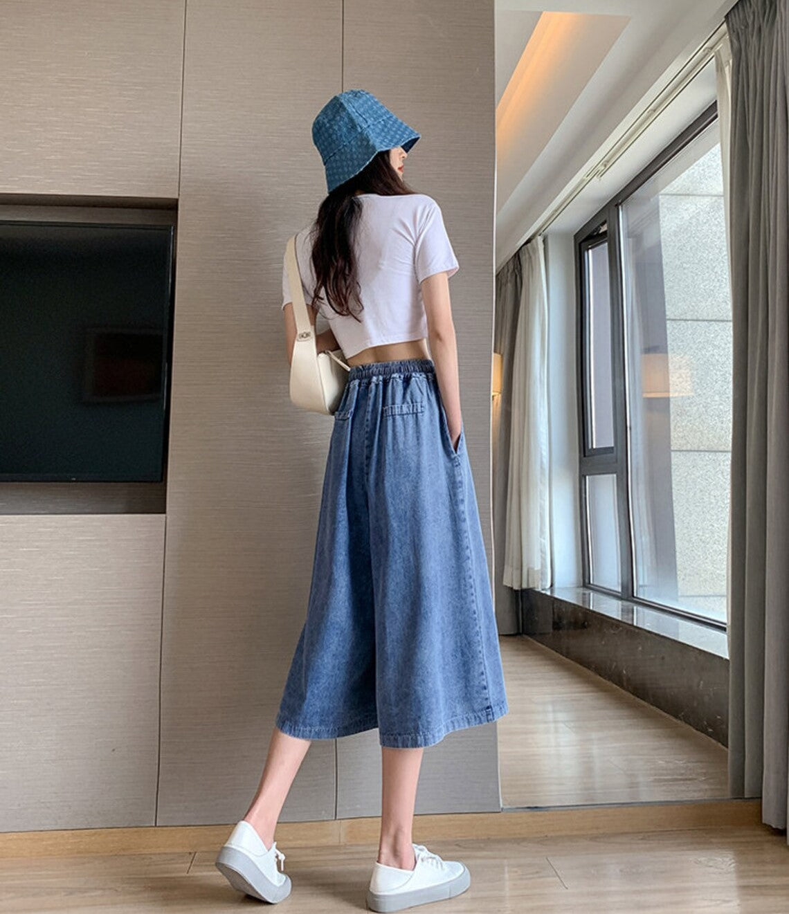Frau in weißem T-Shirt, blauer Jeansrock, blauem Hut, weiße Sneaker, moderne Wohnung.